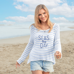 Model wearing coastal-inspired sweater with “Seas the Day” lettering