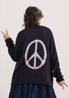 Woman wearing navy cardigan with embroidered peace sign and flower details on the back